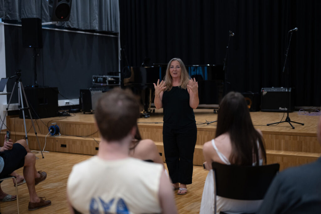 Workshop im Saal: Teilnehmerinnen und Teilnehmer sitzen im Halbkreis vor der Bühne