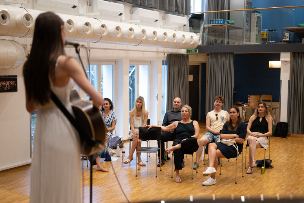 Teilnehmerin mit Gitarre spielt vor der sitzenden Workshop-Gruppe