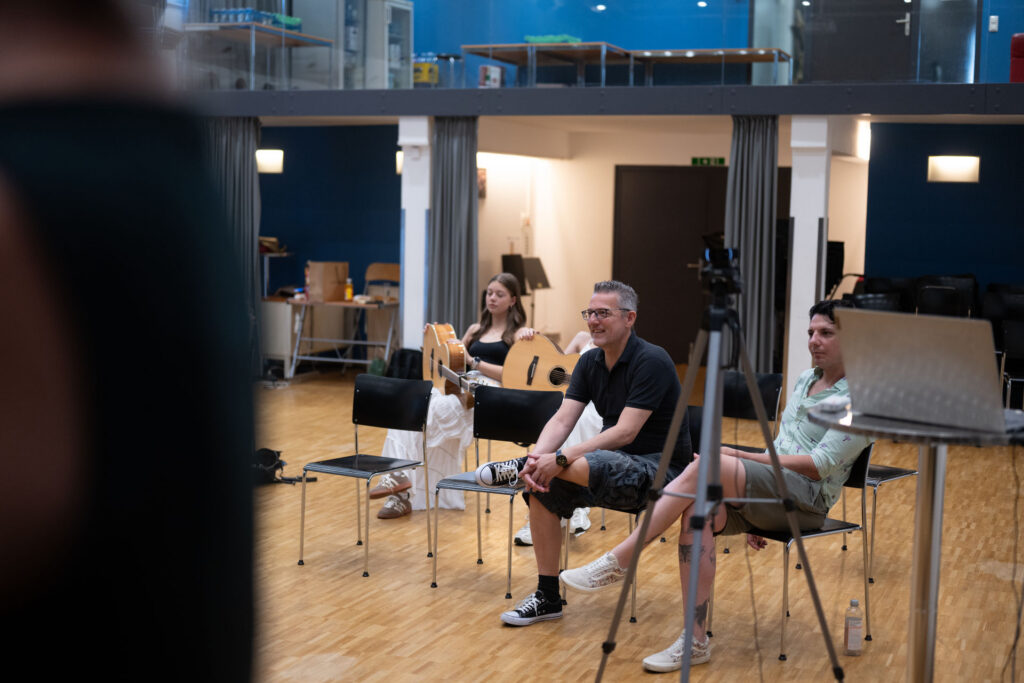 Workshop-Runde im Saal, eine Teilnehmerin mit Gitarre sitzt in der Gruppe